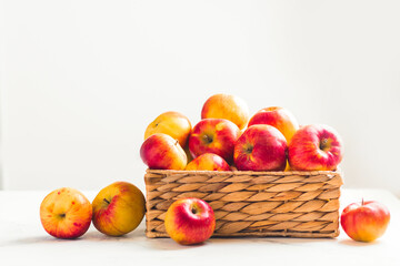 Fresh yellow and red apples in the wicker basket on the white background. Autumn harvesting