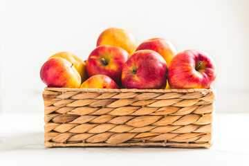 Fresh yellow and red apples in the wicker basket on the white background. Autumn harvesting