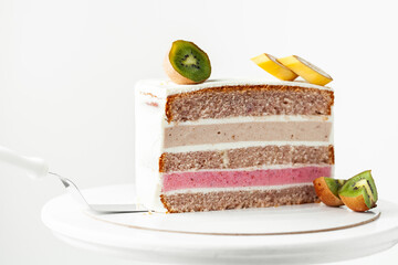 Fruit cake cut on the white background.  Sponge biscuit and fruit mousse layered cake. Tropical fruit cake