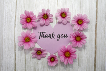 Background with pink flowers, heart card, handwriting text thank you, on white wood. Concept for mothers day, valentines day, womens day.