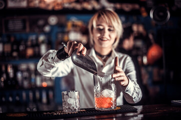Pretty woman bartender intensely finishes his creation while standing near the bar counter in nightclub