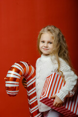 Little cute girl in the studio on a red background with Christmas toys