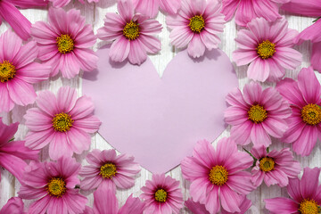 Background with frame of pink flowers and heart card on white wood. Concept for mothers day, valentines day, womens day.