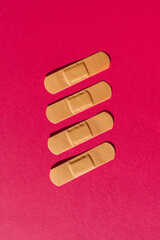 Four plasters patches form a pattern on a pink flat background