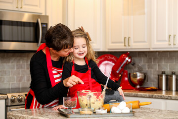 Toddler girl in red apron baking chocolate chip christmas cookies at holidays with grandmother in kitchen