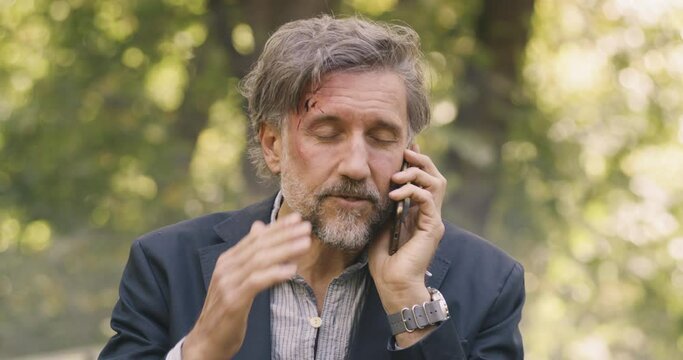 Injured middle aged man speaking on smartphone after car crash
