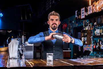 Bearded bartender formulates a cocktail behind the bar