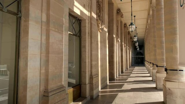 Footage of hung lamps and columns at a palace called "Domaine National du Palais Royal" in Paris. It is a sunny summer day. Camera moves forward.