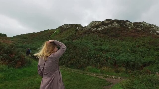 The girl in long coat walks down the hill. View of a young woman from the back. Tracking in Ireland near Dublin. High quality FullHD footage video.