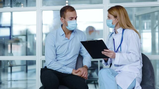 In hospital corridor man with medical mask sitting speaking with woman doctor about diagnosis during consultation. Patient clinic covid coronavirus illness. Slow motion