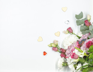 Flat lay with a bouquet of fresh flowers on a white background and small decorative hearts. Horizontally with space.