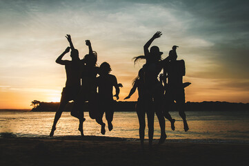 silhouettes of many people jumping for joy on the sand on the beach with the sunset behind them
