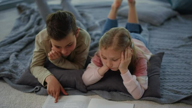 Brother and sister studying with classbook at home. Siblings touching book pages
