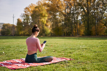 Woman using a mobile phone after practicing yoga in the park - relaxing in nature
