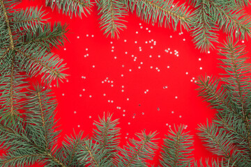 Branches of a Christmas tree on a red background with silver confetti stars. Christmas and new year concept. Copy space.
