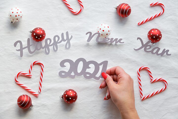 Happy New Year 2021 text. Christmas decorations - hearts from candy canes, red white trinkets on white textile background.