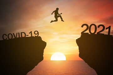 silhouette man jump from the mountain from 2020 which covid-19 spread to 2021 years with the sunset or sunrise background. Happy and success growth with new year 2021 concept