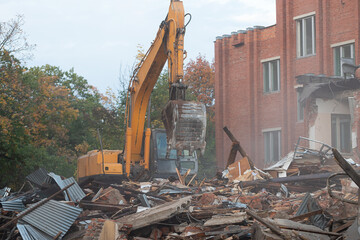 Fototapeta premium a large excavator breaks down the house, demolishing a building in the city