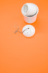 Vertical shot of a white tea strainer and an infuser isolated on an orange background