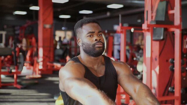 African american man bodybuilder with wireless headphones exercising on seated low row machine at gym