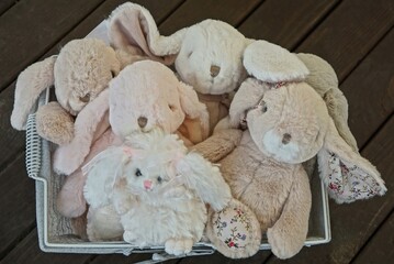 many of soft plush toys pink and gray hares in a box on a brown table