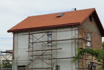 repair and insulation of a gray wall of a large private house under a red tiled roof against the sky