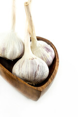 three garlic head large and mature stands in a wooden bowl on a white isolated background