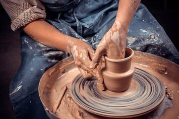 Craftsman siting on bench with pottery wheel and making clay pot. National craft. Close-up. - obrazy, fototapety, plakaty