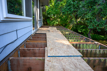 Summer construction, outdoor deck under construction, old support joists with plywood walkway on top
