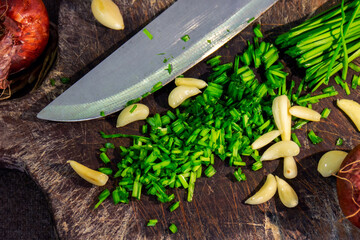 Top view of sliced onion chives, garlic, and onions on a wooden chopping board