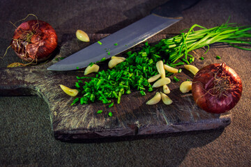 High angle shot of sliced onion chives, garlic, and onions on a wooden chopping board