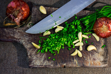 High angle shot of sliced onion chives, garlic, and onions on a wooden chopping board