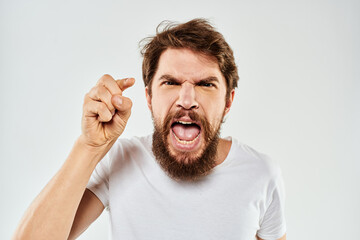 Emotional bearded man in a white t-shirt gestures with his hands light background