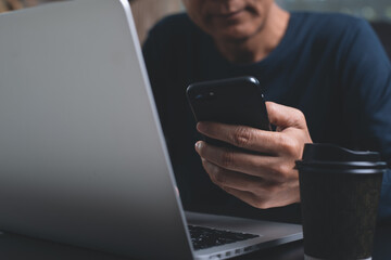 Man using mobile phone surfing the internet during working on laptop computer at home office