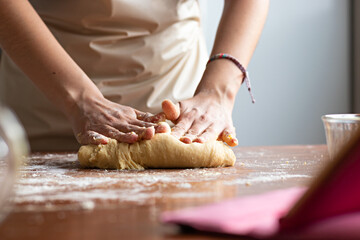 Hands of a young woman, kneading dough to make bread on top of a wooden table