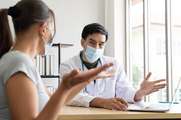 Woman wearing face mask sitting and talking to the professional psychologist while wearing face mask conducting a consultation and using computer notebook during coronavirus or COVID 19 outbreak