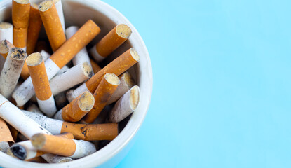 Cigarettes buds in a transparent ashtray on  blue background.