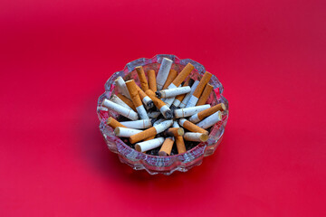 Cigarettes buds in a transparent ashtray on red background.