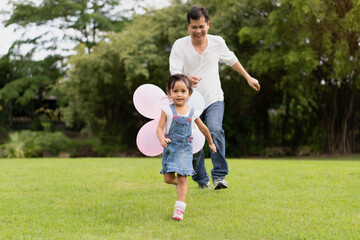 Fototapeta premium Asian father and daughter are playing the balloons and they running and laughing together with fully happy moment in the park, concept of outdoor activity in family lifestyle.