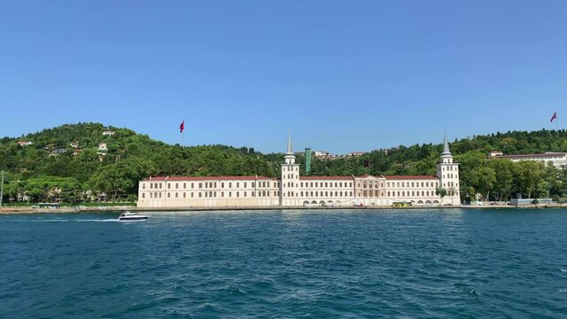 Footage of yacht passing in Kandilli / Cengelkoy area of Istanbul on Bosphorus strait. Kuleli military school is in the view. Beautiful scene. It is a sunny summer day. Camera moves forward.