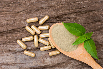 Herbal medicine capsules and herbs powder in wooden spoon with basil leaf on rustic wood table background. Top view. Flat lay. 