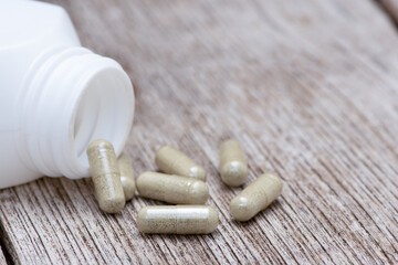 Green natural herbal powder capsules in white bottle on wood