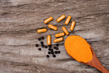 Turmeric ground or tumeric powder in wooden spoon with curcuma capsules and black pepper ( peppercorns, piperine or piper nigrum ) isolated on wood 