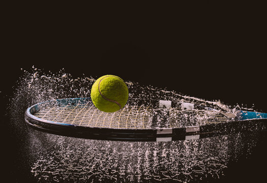 Closeup shot of a tennis ball and racket with a splash of water isolated on a dark background
