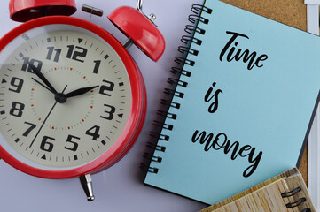 Flat lay view of alarm clock, white board and notebooks written with text Time Is Money. Time money business concept.