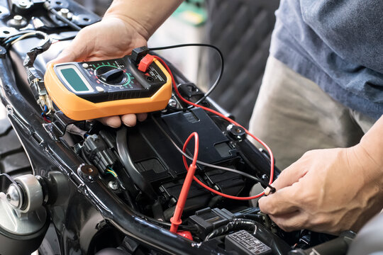 mechanic using multimeter to check the voltage level on motorcycle battery at garage, Maintenance and repair concept - Powered by Adobe