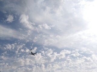 a plane passing through a beautiful blue sky with fluffy clouds and bright sun shining.