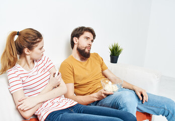 Fototapeta premium A woman in a striped T-shirt and a man on the couch watching the TV in a bright room