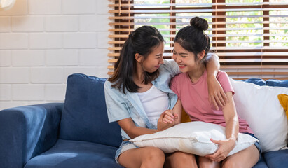 Happy asian lesbian couple holding hand and hug together at sofa in living room at cozy home