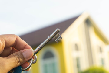 Woman's hand was holding a key and there was yellow house as the background.